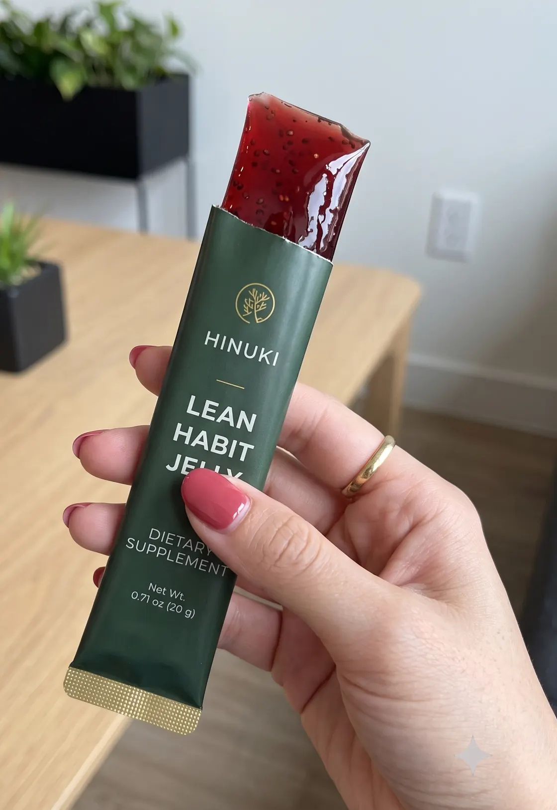 A torn-open Hinuki Lean Habit Jelly stick held in one hand, showing the red pomegranate gel inside the 20 g green and gold sachet.